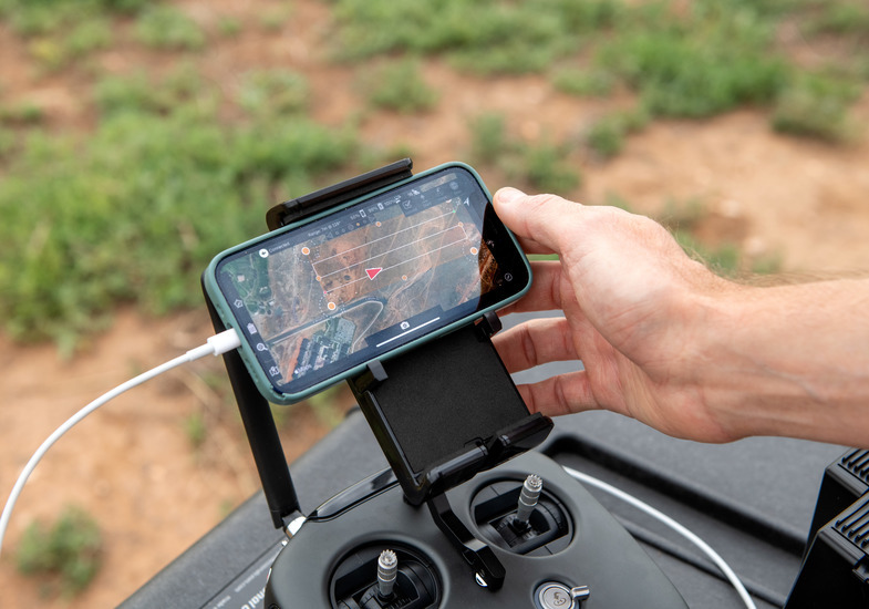 A drone controller holds a phone displaying a map
